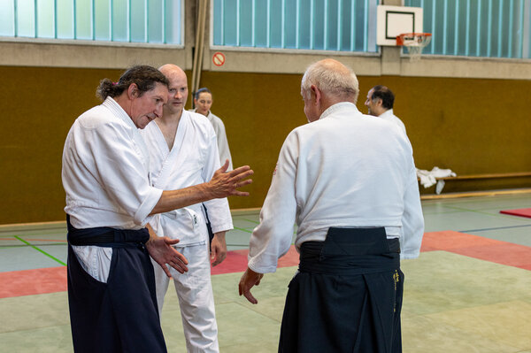 Trainer erklärt einem Teilnehmer eine Aikido-Technik und unterstützt ihn während des Trainings.